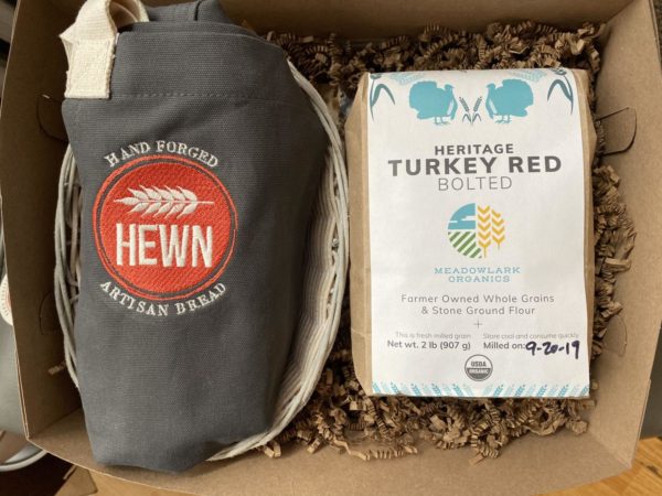 package with an apron that features the hewn logo and says "hand forged artisan bread" and bag of Heritage turkey red bolted, meadowlark organics, farmer owned whole grains & stone ground flour